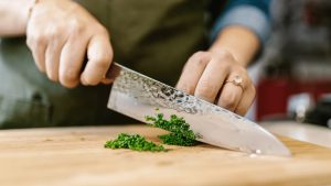 a profesional chef knife being used to chop up green on a wooden cutting board